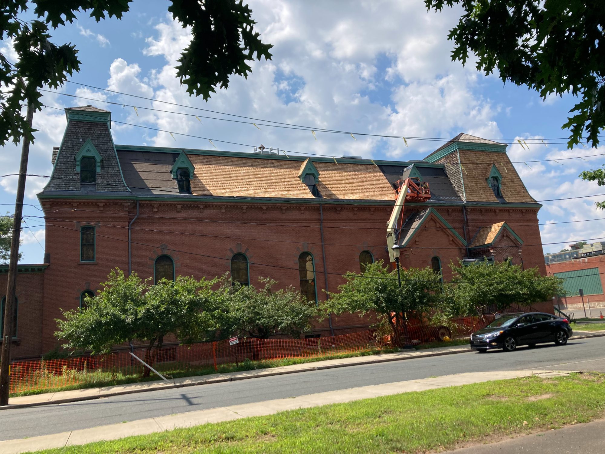 Cheney Hall in Manchester during the re-roof: new cedar shingles across the mansard roof and dormers, with a boom lift at the gable