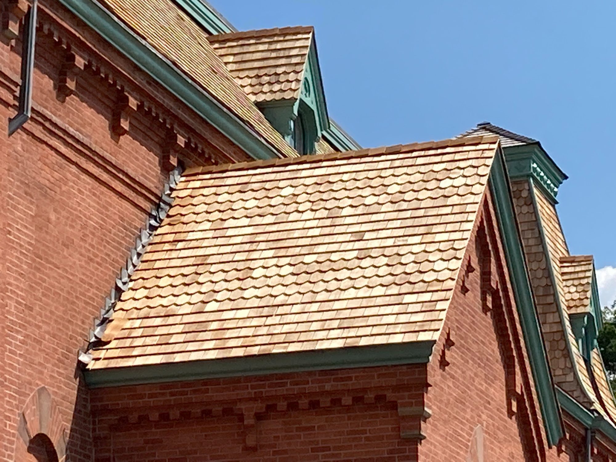 Close-up of the new hand-laid cedar shingles meeting the corbelled brick cornice and green-trimmed dormers