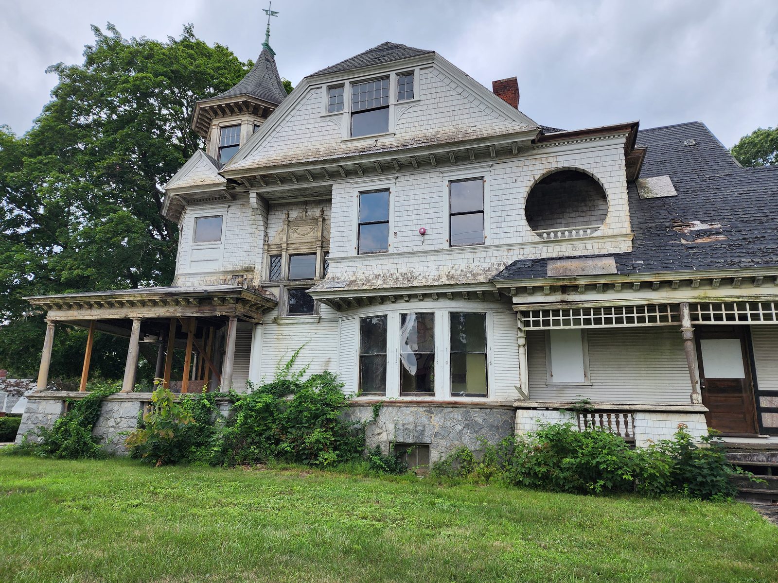 Right elevation before restoration: corner turret with conical roof and weathervane, round-arched attic alcove, bay window with a torn curtain, failing slate roof and a porch held up on temporary posts