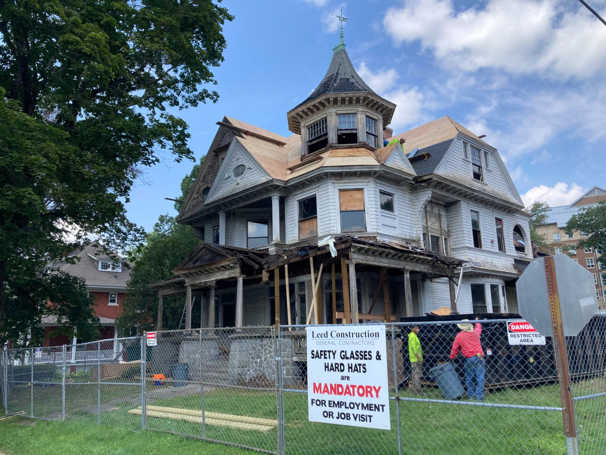 347 Prospect Street mid-restoration behind construction fencing, with the porch structure stripped to its framing and the turret re-roofed