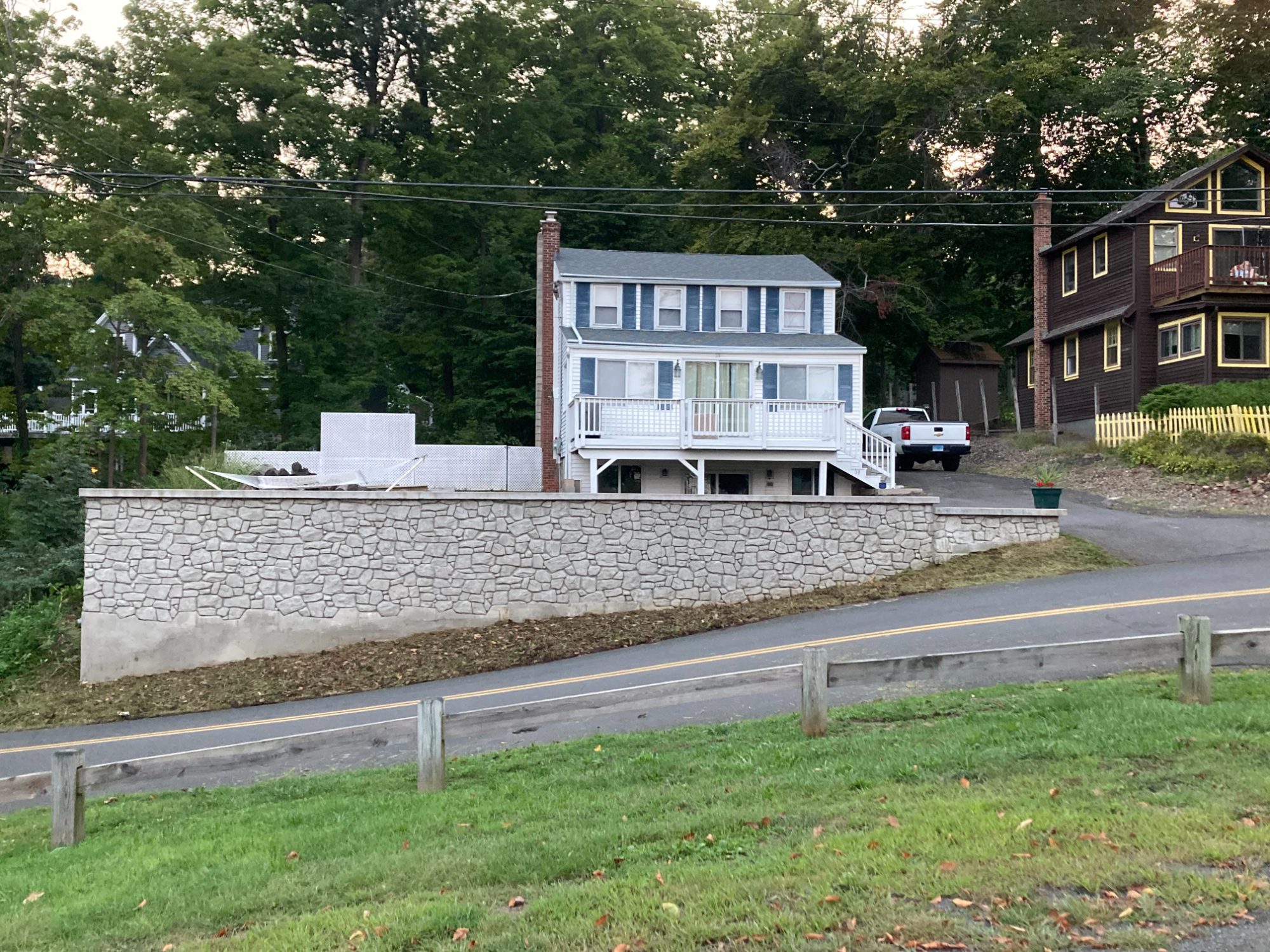 New form-lined concrete retaining wall with a stone-textured face and concrete cap below a hillside home in Middlefield