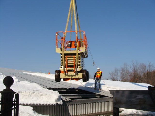 Scissor lift being lowered onto the snow-covered basin roof while a worker guides it