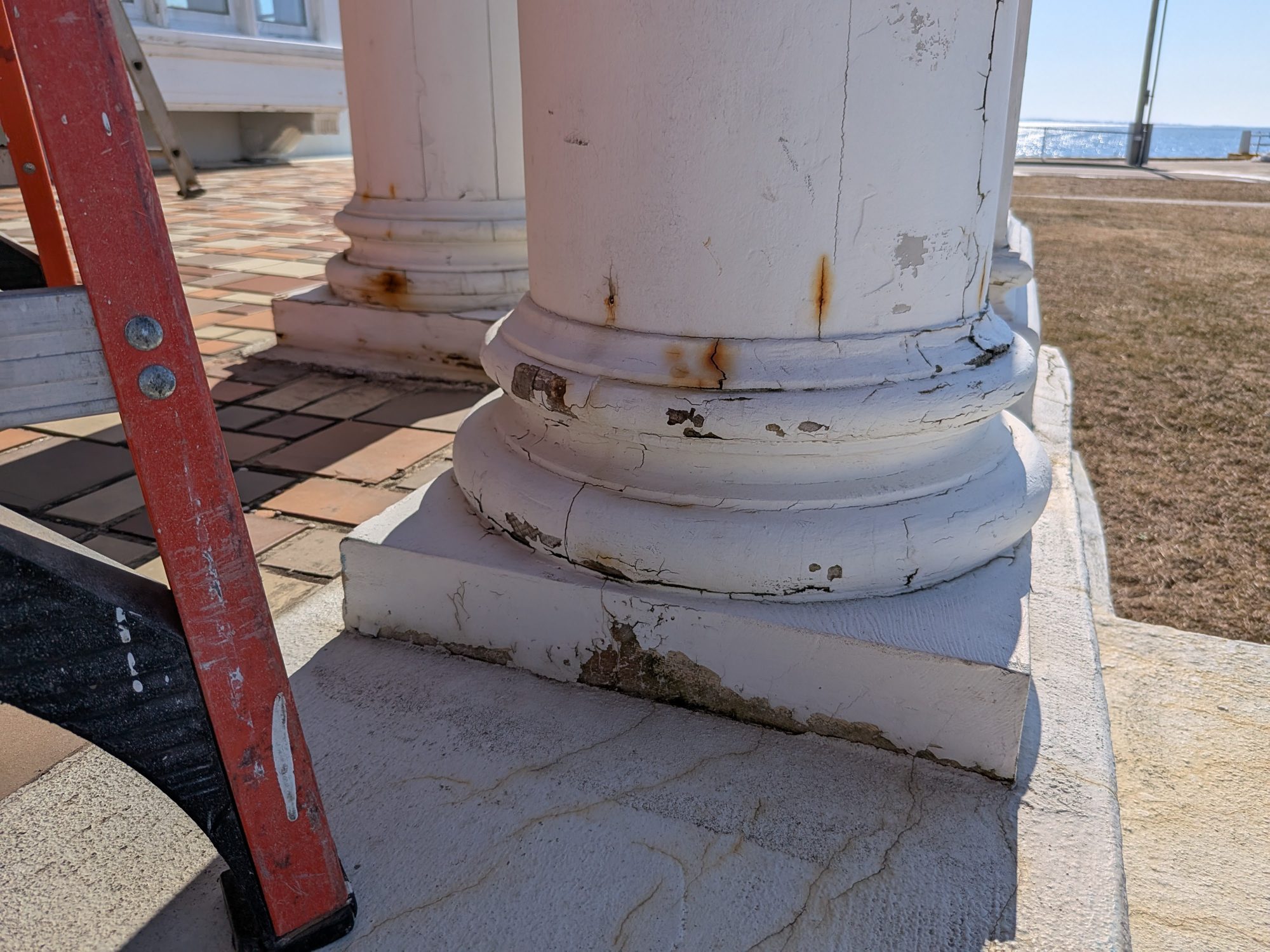 Porch column base before restoration, with cracked and peeling paint, rust stains and rotted wood at the plinth